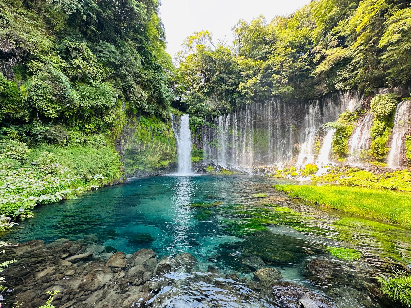 Wide view of Shiraito Falls cascading over a mossy cliff into a clear pool
