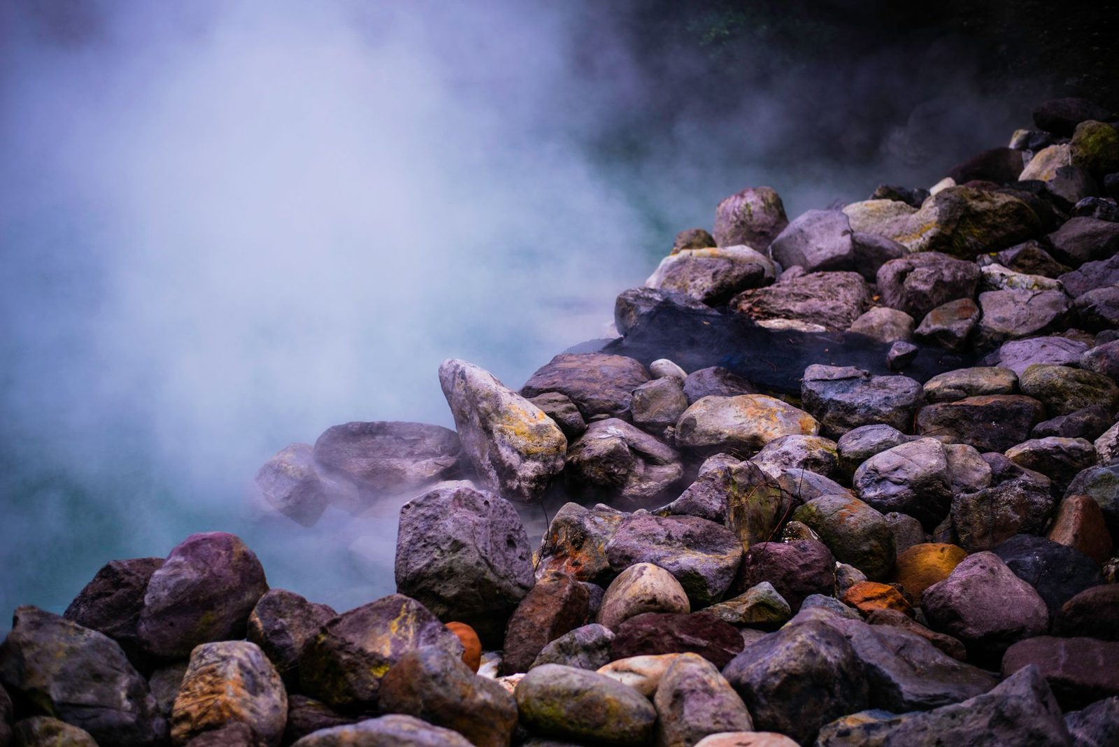 Illustrative photo: A scenic view of steaming geothermal hot springs surrounded by colorful boulders, creating a tranquil natural scene.