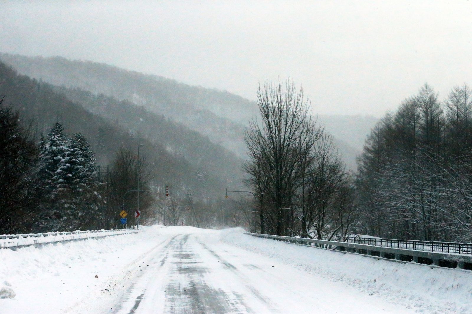 Illustrative photo: A serene winter scene of a snowy road winding through a mountain landscape under a cloudy sky.