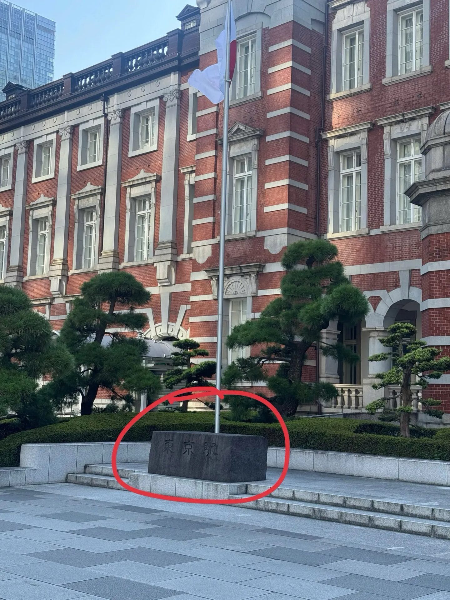 Tokyo Station stone marker (東京駅) under the flag pole, Marunouchi side — meeting point circled in red